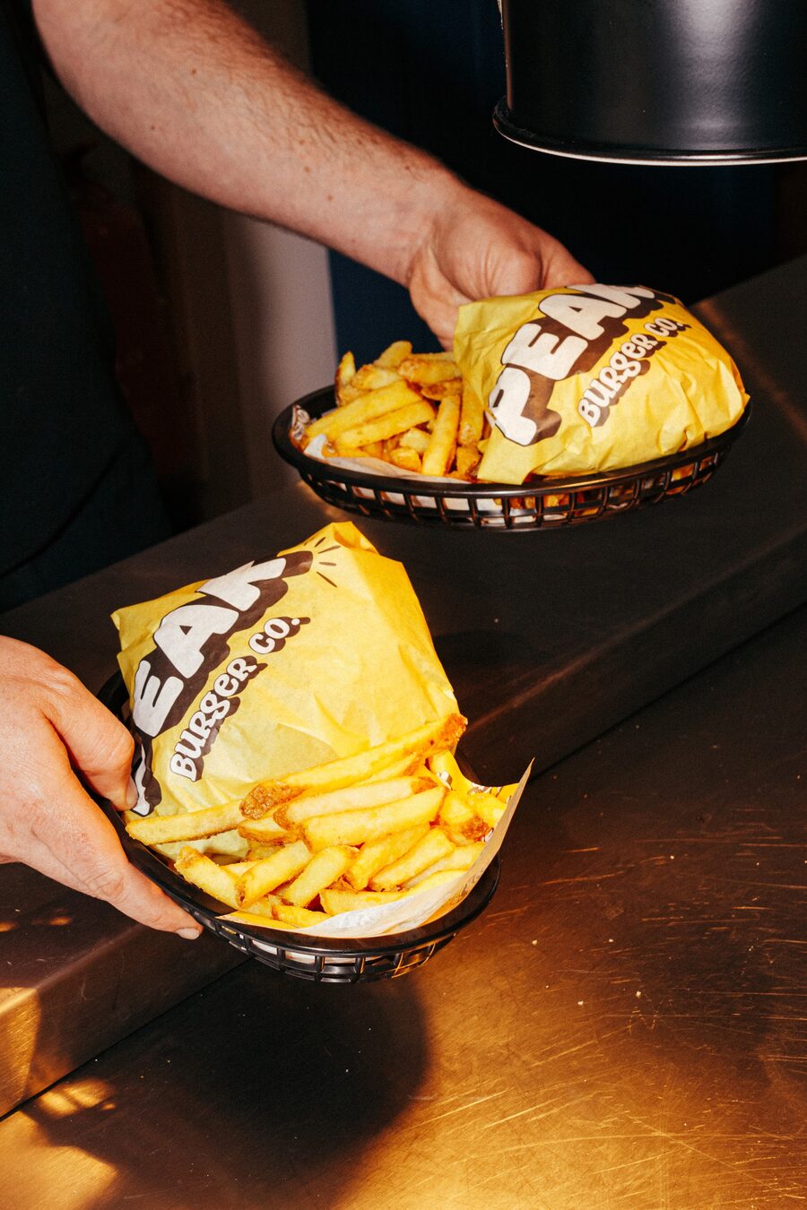 Two Peak Burger Co burgers wrapped in branded paper with fries, ready to serve