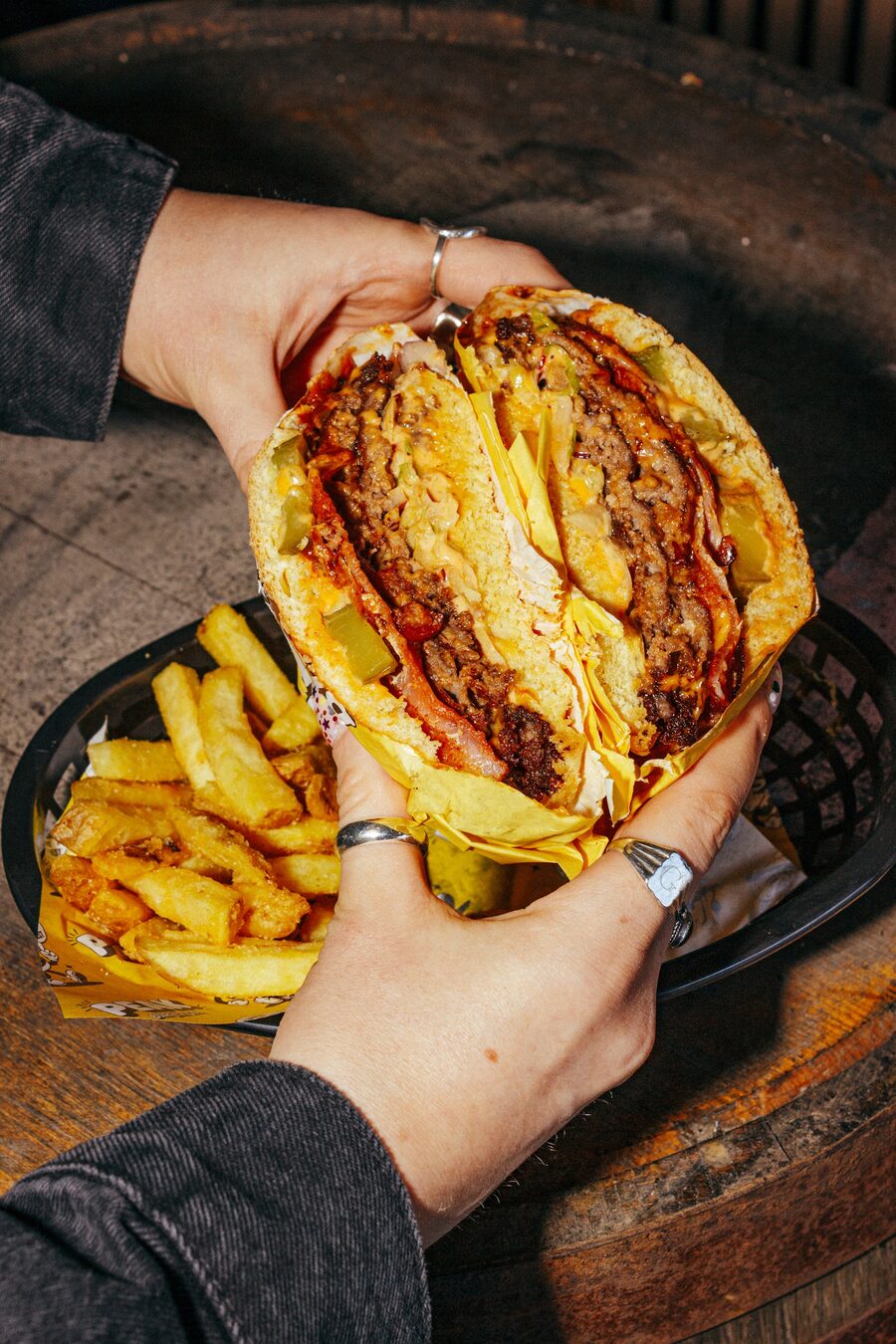 Hands holding a cross-section Peak Burger Co smash burger with fries