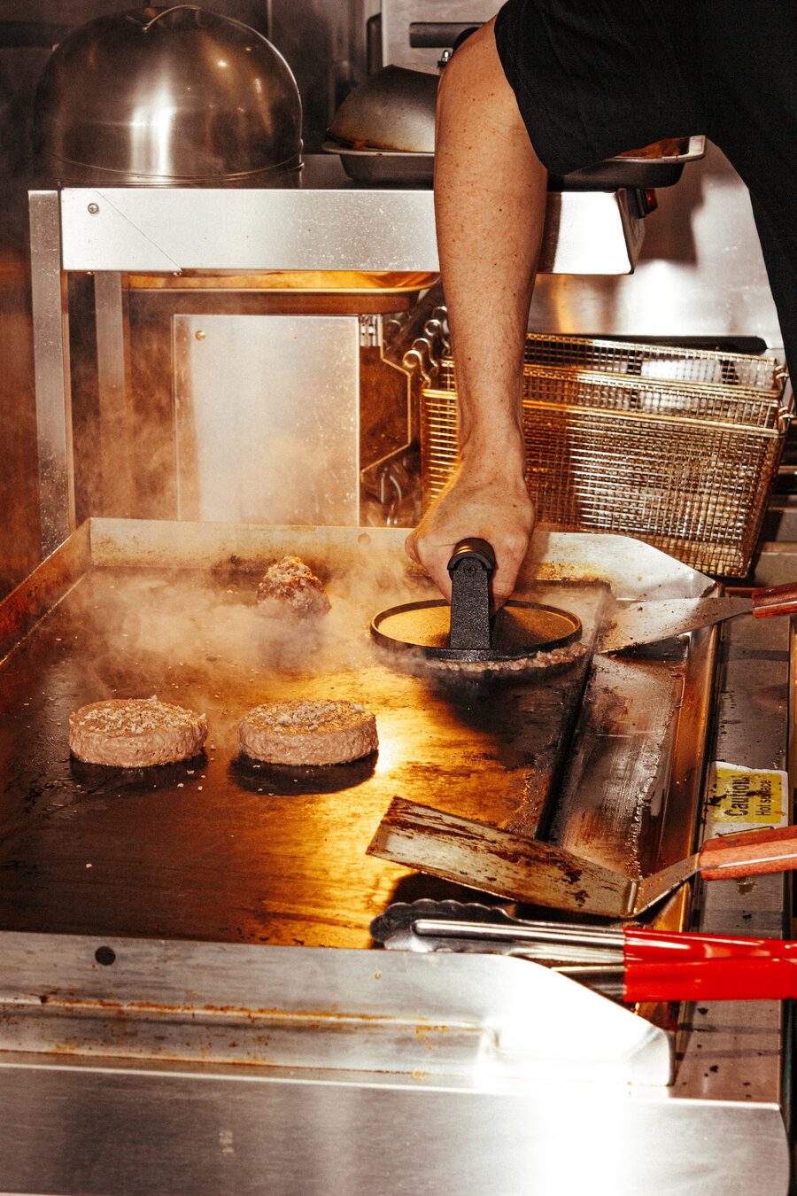 Beef patties being smashed on the hot griddle at Peak Burger Co